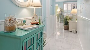 A teal-colored console table with decorative items, a mirror, and a ceiling fan in a well-lit hallway.