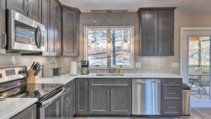 A modern kitchen with dark cabinets, stainless steel appliances, and a large window overlooking a snowy landscape. - Massanutten Resort Home w/ Deck + Mountain Views! (McGaheysville)