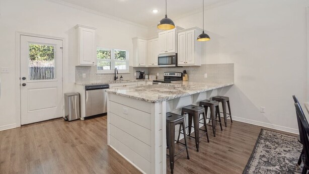 A modern kitchen with white cabinetry, a granite countertop, and bar stools.