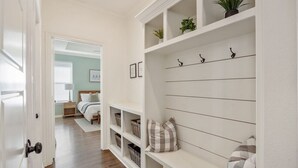 A hallway with white shelves, a bench, and a door leading to a bedroom.