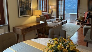 A living room with a sofa, a coffee table, a lamp, and a painting on the wall. - Amazing Lake Views from Large Terrace.  Swimming and Boat Dock on Property (NESSO)