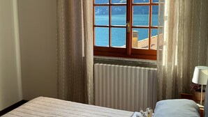 A bedroom with a large bed, a window with a view of the sea, and a radiator. - Amazing Lake Views from Large Terrace.  Swimming and Boat Dock on Property (NESSO)