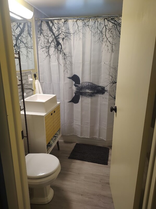A bathroom with a toilet, a sink, a mirror, and a shower curtain with a tree design.