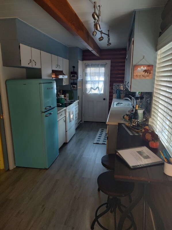 A compact kitchen with a vintage teal refrigerator, wooden cabinets, a small dining area with stools, and a window with a curtain. - You'll Love this Comfortable Log Cabin on Popular Big Springs Rd. (Westwood)