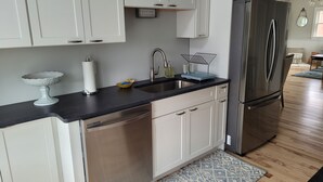 A modern kitchen with stainless steel appliances, white cabinetry, and a black countertop. - Blue Moon Carriage House (Narragansett)
