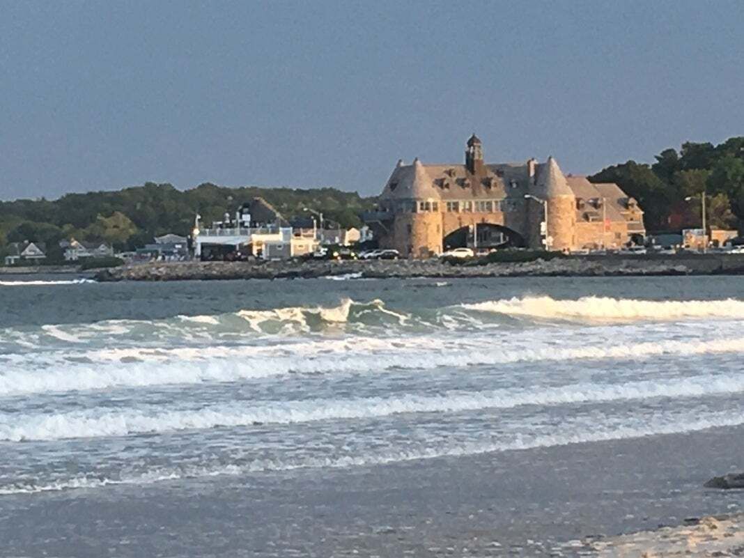 A coastal building with a prominent tower, situated near a beach with waves.
