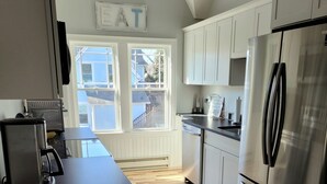A modern kitchen with a large window, a refrigerator, and a dining area. - Blue Moon Carriage House (Narragansett)