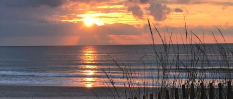 A beach with a wooden fence in the foreground and a sunset over the ocean.