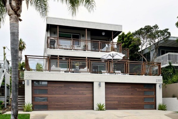 Una casa moderna de dos pisos con balcón, garaje y un gran paraguas.
