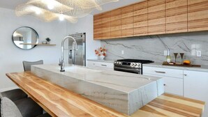 A modern kitchen with a central island, stainless steel appliances, wooden cabinets, and a marble backsplash. - Luxury Cardiff By-the-sea Ocean View Parkhouse (Cardiff-by-the-Sea)
