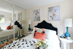 Un dormitorio con una cama grande, dos mesitas de noche, un espejo y obras de arte con motivos florales en las paredes.