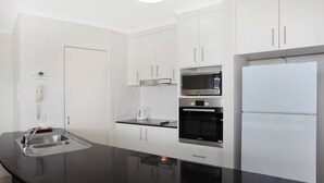 A modern kitchen with white cabinets, a black countertop, a Bosch oven, a microwave, and a refrigerator.