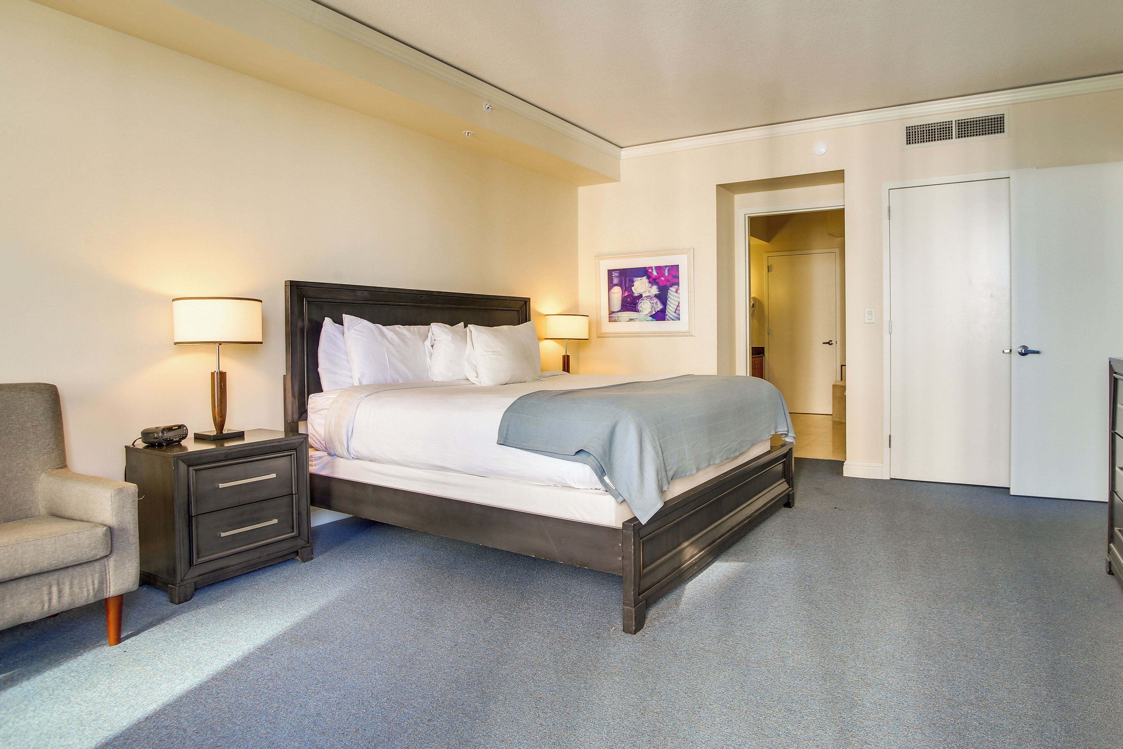 A hotel room with a bed, a nightstand, a chair, and a door.
