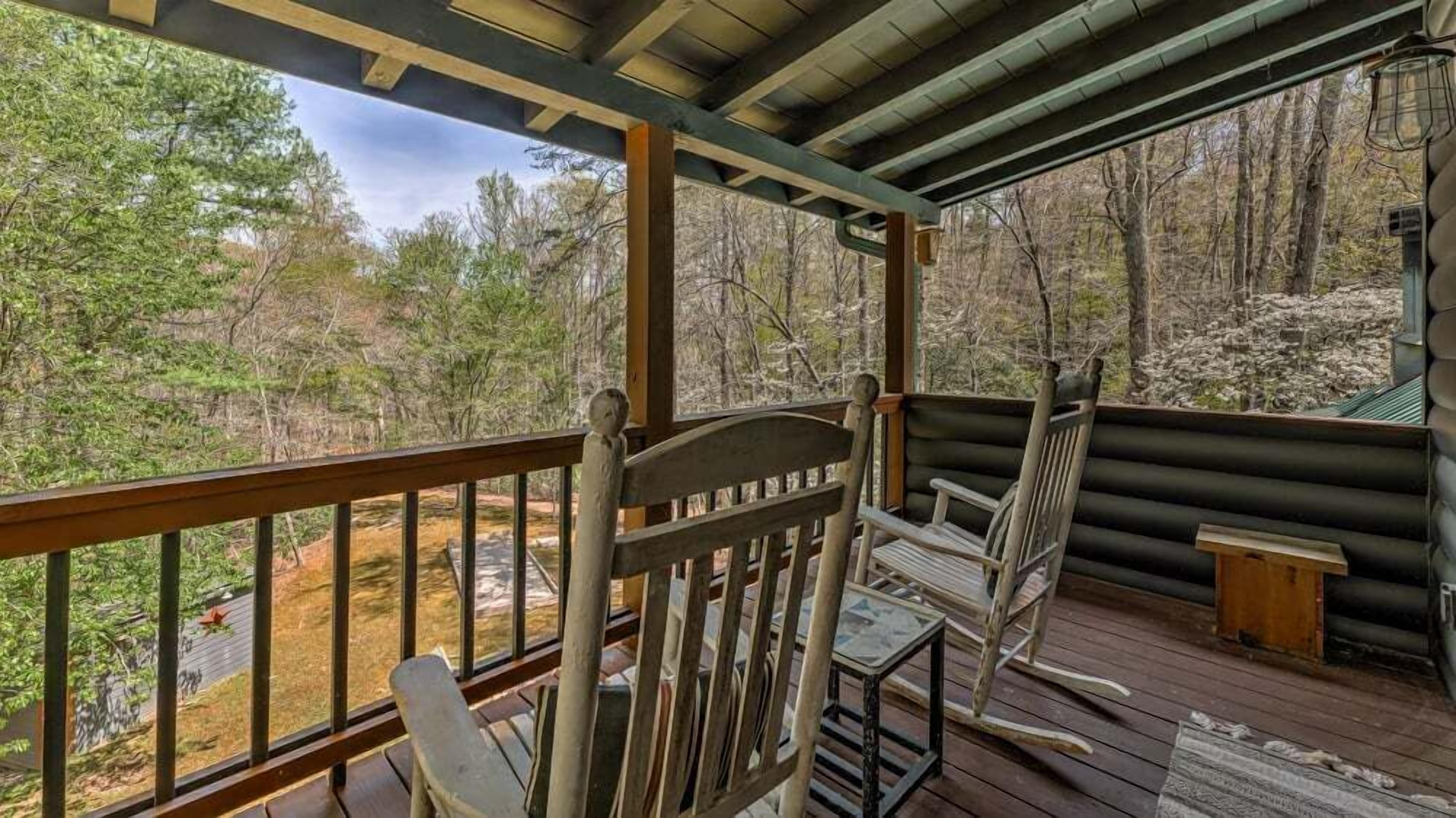 A wooden deck with a railing, two rocking chairs, and a small table.