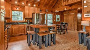 Interior rústico de una cabaña de madera con cocina, comedor y un ventanal con vistas al bosque.