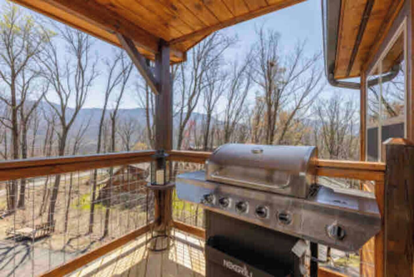 Un balcone con griglia, ringhiera in legno e vista su alberi e montagne.