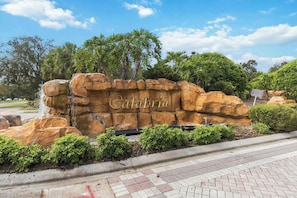A large rock sign with the name 'Calabria' in the center, surrounded by greenery and a paved walkway.
