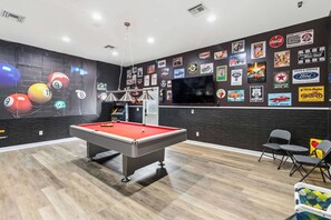 A billiards room with a pool table, a television, and various automotive-themed wall stickers.