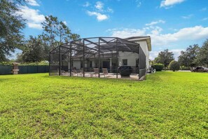 A covered outdoor seating area with a metal frame, a lawn, and a building in the background.