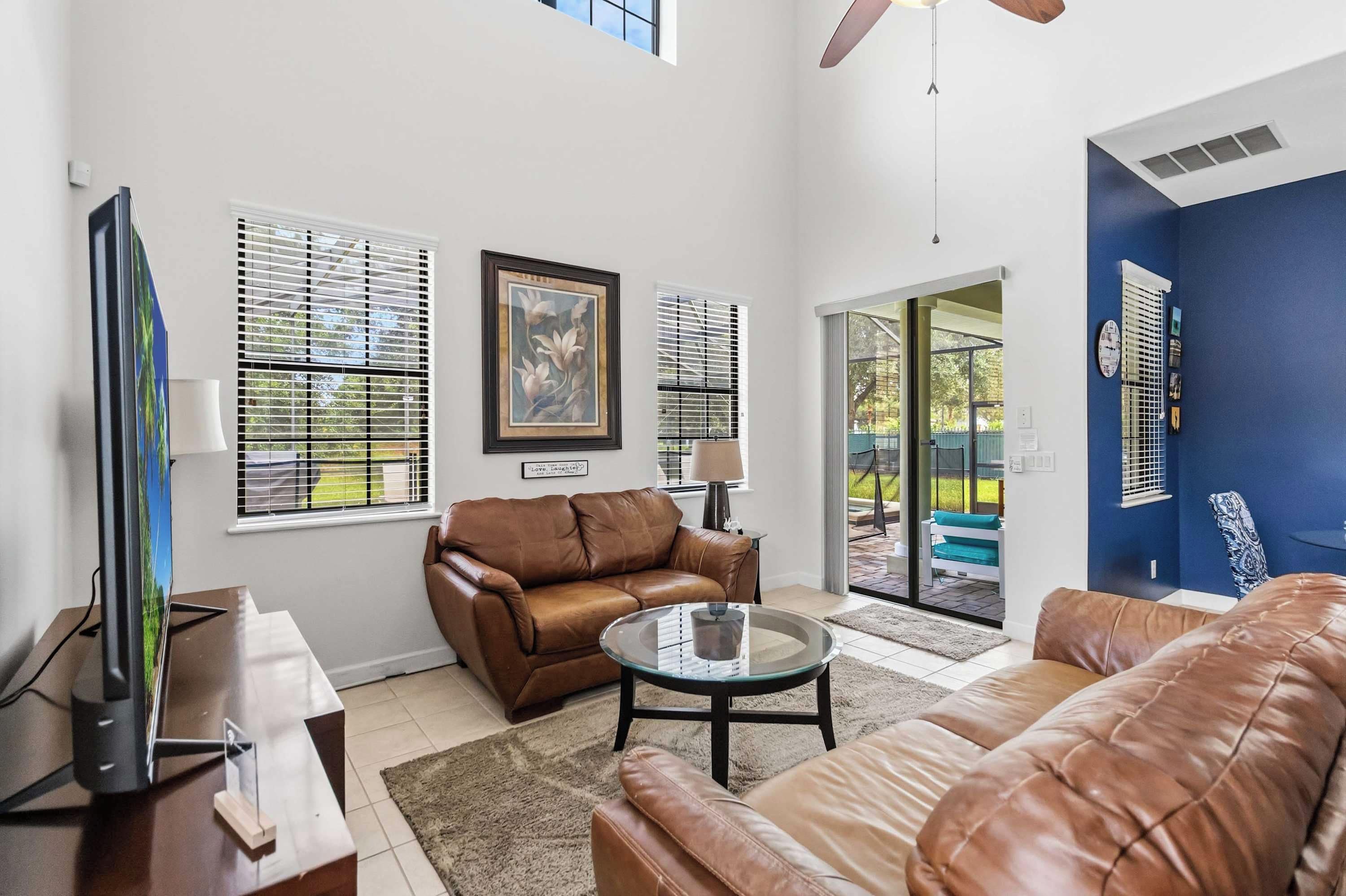 A living room with a brown leather sofa, a glass coffee table, and a television on a stand.