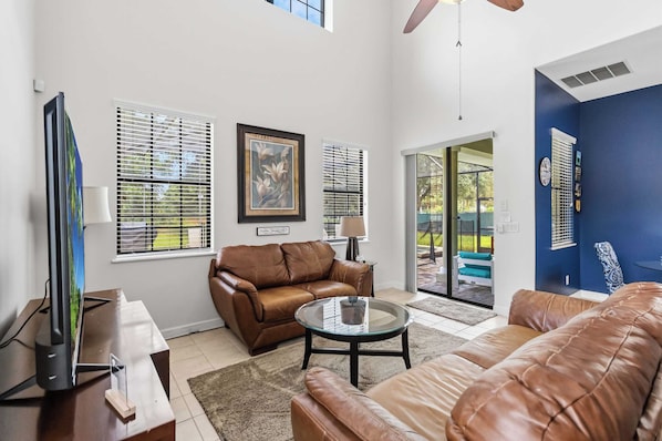 A living room with a brown leather sofa, a glass coffee table, and a television on a stand.