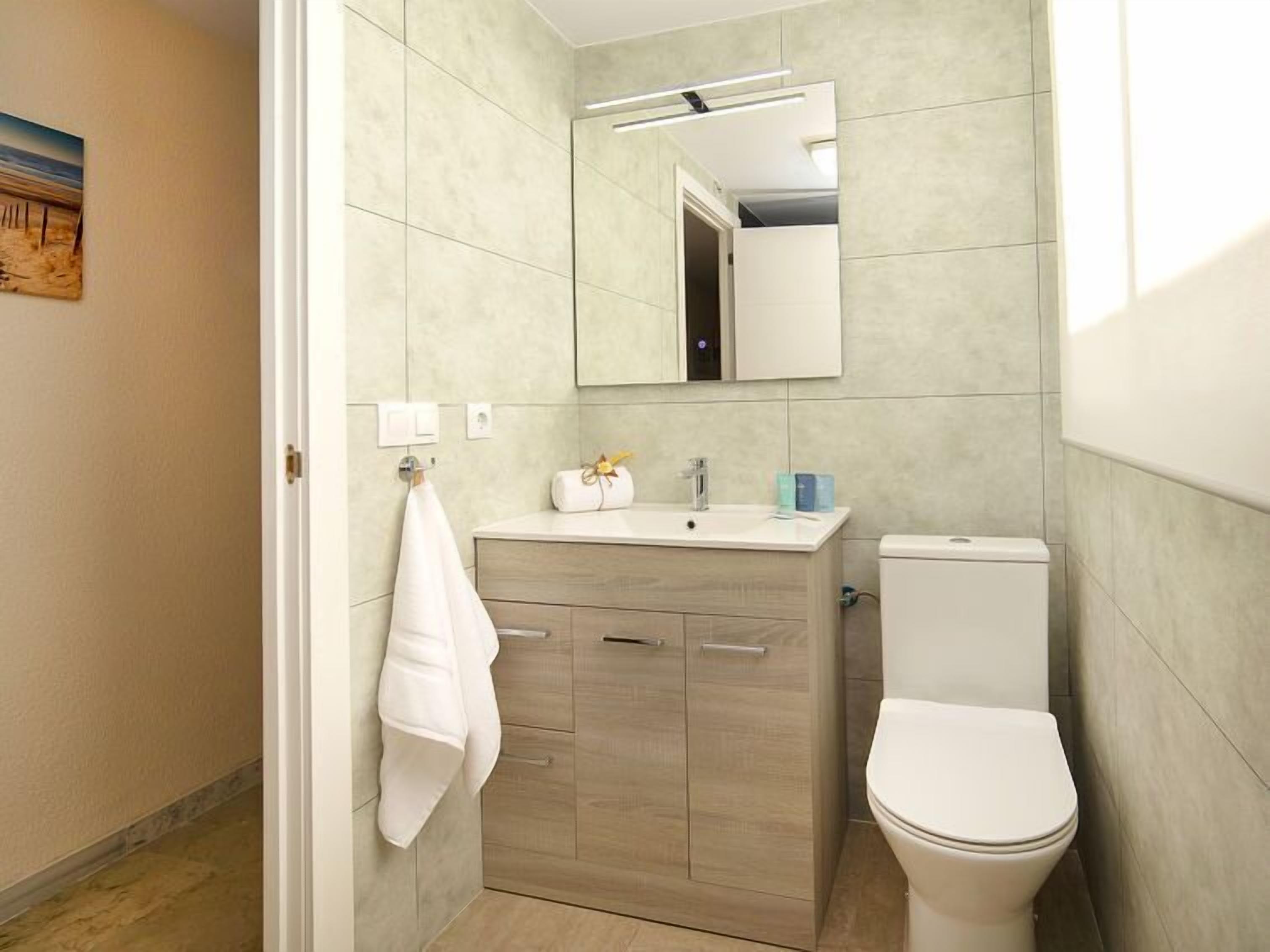 A modern bathroom with a wooden vanity, a white toilet, and a mirror above the sink.