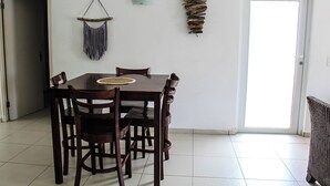 Una zona de menjador amb taula i cadires de fusta, una decoració penjada a la paret i una porta a la dreta.