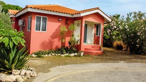 Una casa vermella amb teulada, un porxo i un jardí ple de plantes i flors diverses.