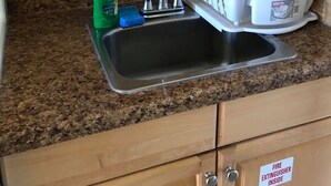 Eine Küche mit Granitarbeitsplatten, einer Edelstahlspüle, Holzschränken und einem Schild für Feuerlöscher.