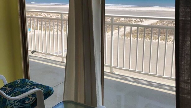Ein Balkon mit Blick auf den Strand, weiße Stühle und ein Glastisch.