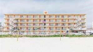 Ein mehrstöckiges Hotel mit Balkonen, einer Flagge und Blick auf den Strand.