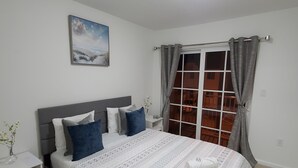 A neatly arranged bedroom with a bed, a bedside table, a nightstand, a window with curtains, and a ceiling light.