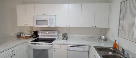 A modern kitchen with white cabinets, a microwave, a stove, a dishwasher, and a sink.
