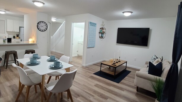 A modern living room with a dining area, a staircase, a kitchen, and a TV mounted on the wall.