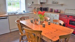 Une cuisine avec une table en bois, des chaises, un four rouge et une fenêtre donnant sur un paysage verdoyant.