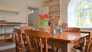 Un coin repas avec une table en bois, des chaises et un vase rempli de tulipes rouges. On y trouve également une bibliothèque avec de la verrerie et une fenêtre donnant sur un paysage verdoyant.