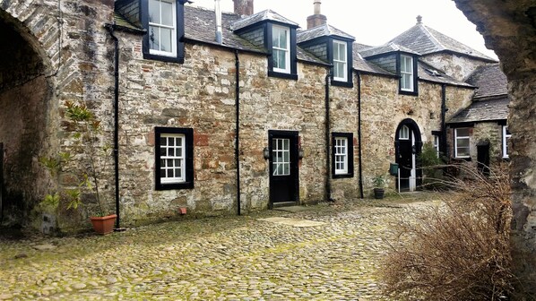 A stone building with multiple windows and doors, a cobblestone courtyard, and a small potted plant.