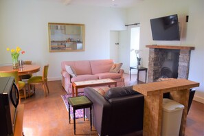 Ein Wohnzimmer mit einem karierten Sofa, einem Couchtisch, einem Fernseher über einem Kamin und einem Essbereich mit Tisch und Stühlen.