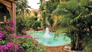 Un jardín tranquilo con una fuente central, abundante vegetación y una pérgola de madera.