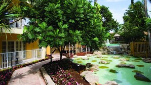 Un hotel con un sendero pavimentado, una fuente de agua con rocas y abundante vegetación.