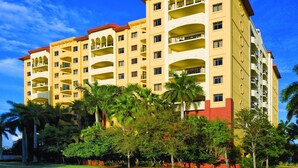 Un hotel de varios pisos con balcones, rodeado de palmeras y vegetación.