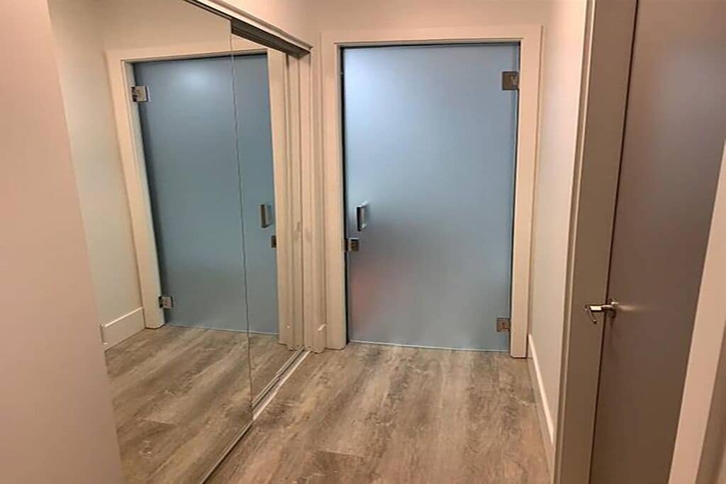 Un couloir avec deux portes : l’une est dotée d’un panneau coulissant en verre et l’autre d’une porte pleine, et les deux sont équipées de poignées.