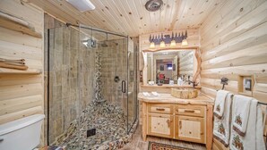 A wooden cabin bathroom with a glass shower, a wooden vanity, and a mirror with a forest-themed light fixture. - Happy Days and Nights - Bear's Den (Harbor Springs)