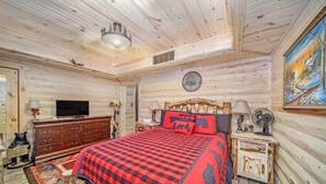 A log cabin bedroom with a bed, dresser, television, and a painting on the wall. - Happy Days and Nights - Bear's Den (Harbor Springs)