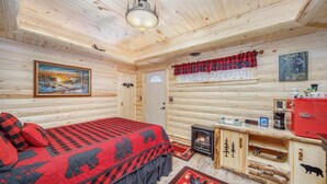 A log cabin bedroom with a bed, a fireplace, a clock, and a welcome sign. - Happy Days and Nights - Bear's Den (Harbor Springs)