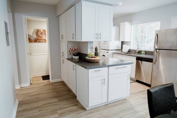 A modern kitchen with white cabinets, a stainless steel refrigerator, and a wooden floor.