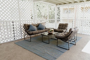 A covered outdoor seating area with a sofa, armchair, and coffee table, separated by a white lattice partition. - FIFA World Cup: NEWLY RENOVATED 2-BEDROOM TOWNHOUSE WITH PRIVATE ROOFTOP DECK REMODELED IN 2022  (p30) (Los Angeles)