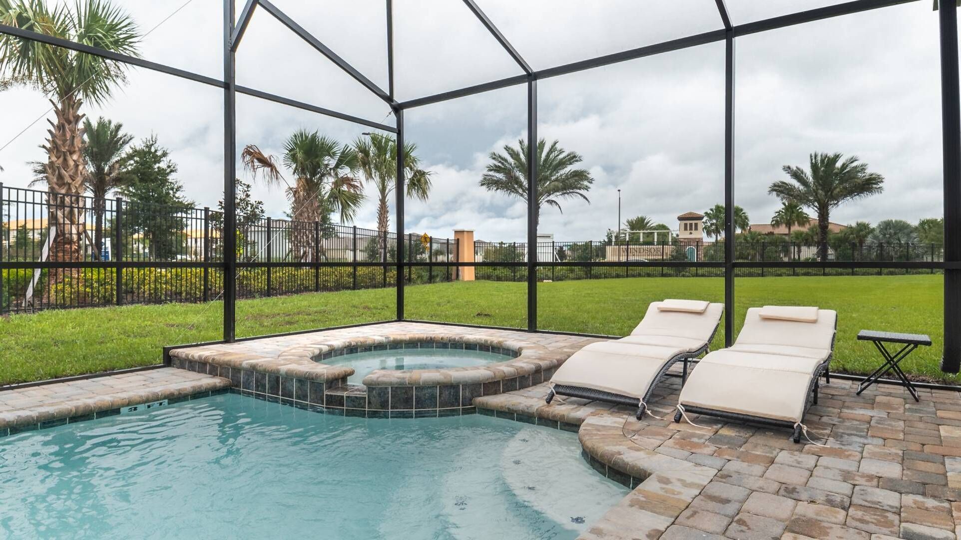 A swimming pool with a hot tub and lounge chairs, surrounded by a glass enclosure and palm trees.