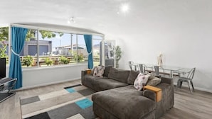 Uma sala de estar moderna com um sofá cinzento, uma mesa de jantar com cadeiras e uma janela grande com cortinas.