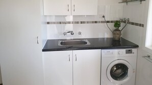 Uma cozinha compacta com armários brancos, bancada preta, pia de aço inoxidável e máquina de lavar com abertura frontal.